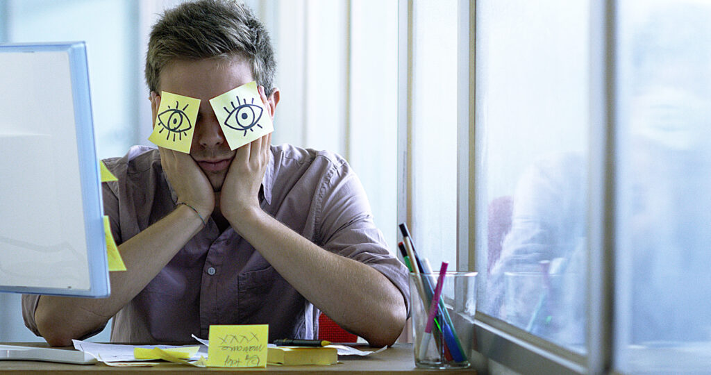 worker resting with post its with hand drawn eyes over face