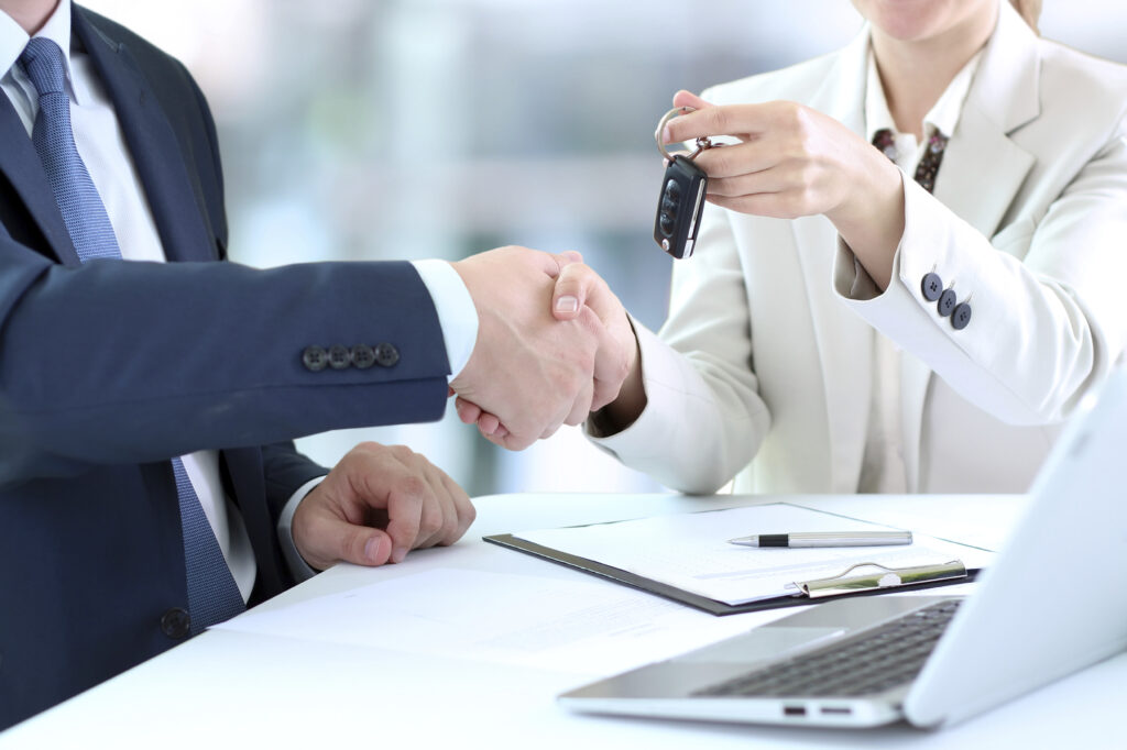 Car saleswoman handing over the keys for a new car to a young bu