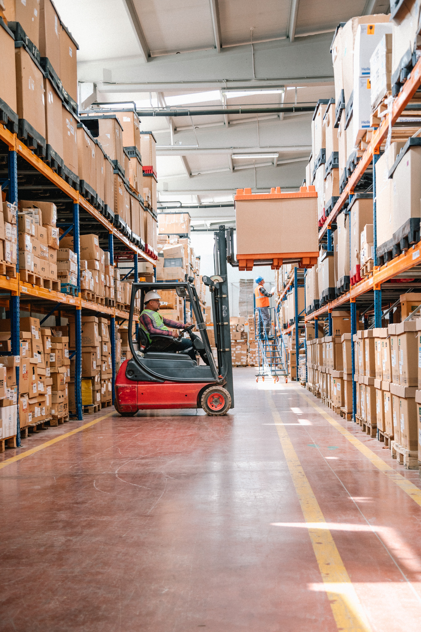 Uniformed Worker Driving and Loading Cardboard Boxes with Forklift Stacker Loader in a Factory Warehouse - KPA Safety Software EHS