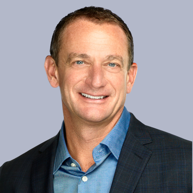 Smiling man in blue shirt and dark blazer.